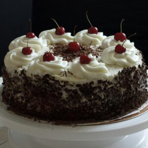 Delicious Black Forest cake topped with whipped cream and cherries on a cake stand.